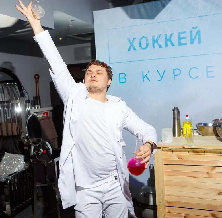 Ведущий научного шоу для взрослых в белом костюме с колбой малинового цвета на сцене