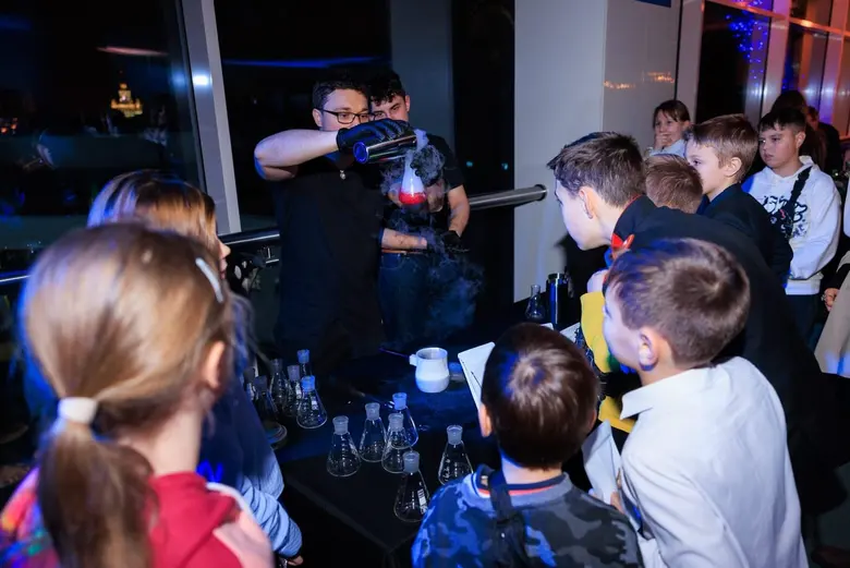 Бармен наливает красный коктейль в колбу, дети обступили бар и ждут свою