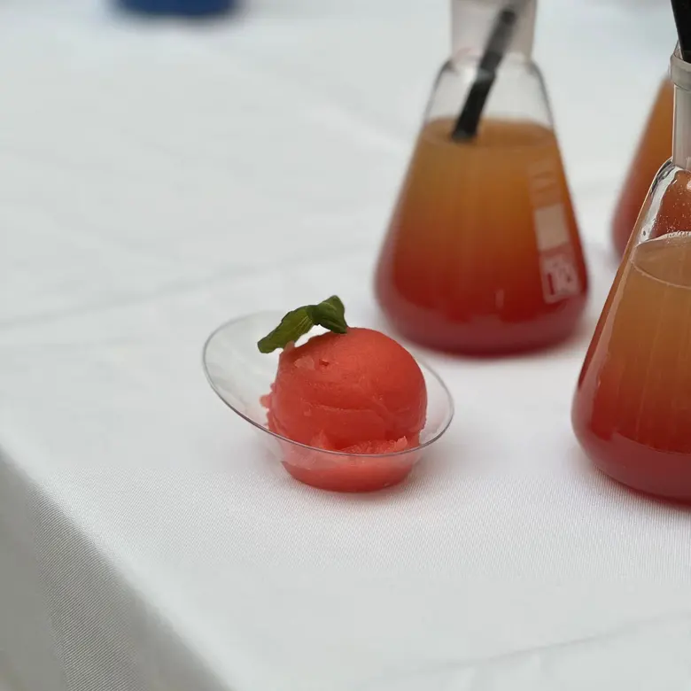 Колбы с коктейлями и красный шарик мороженого из коктейля на белом столе